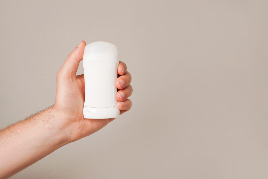 Deodorant Teaches You How To Make Friends Male hand holding white deodorant on gray background. Closeup.