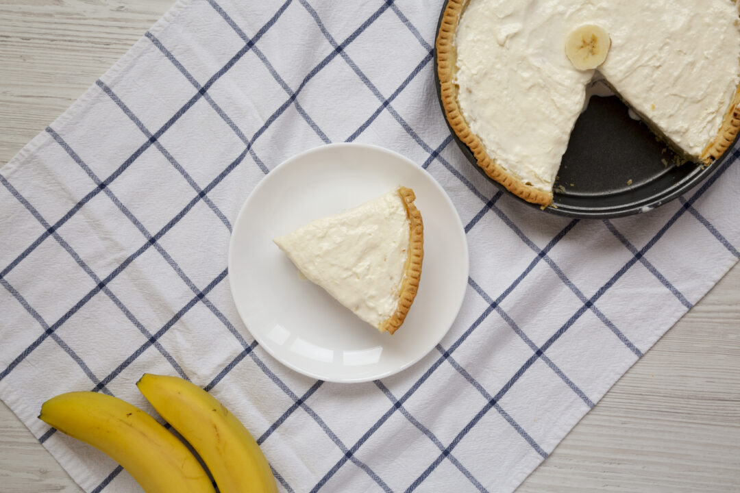 Homemade Tasty Banana Cream Pie on a white wooden table, top vie