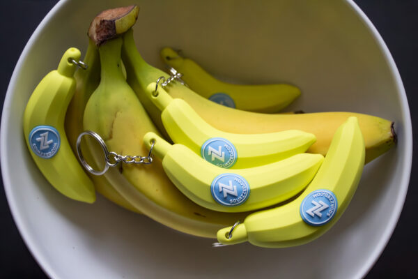 A bunch of bananas joins a group of banana-shaped keychains in a fruit bowl.