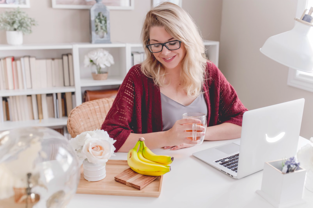A lady working on a banana-branded laptop, gazes lovingly at a bunch of bananas.