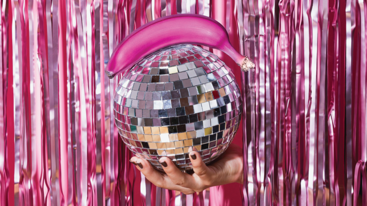 A pink banana being held up on a mirror ball.